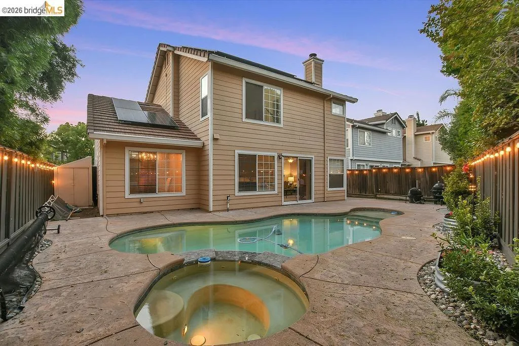 Rear exterior featuring a freeform swimming pool with integrated spa, stamped concrete patio, and mature perimeter landscaping