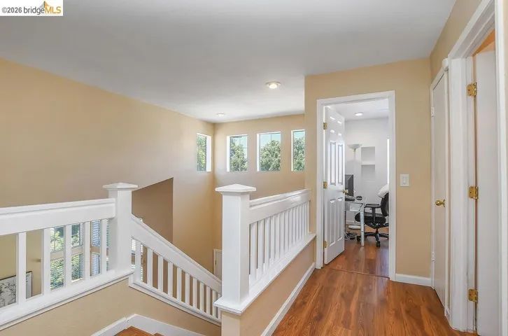 Upper landing with wood-finish flooring, white spindle railings, recessed lighting, and a series of three transom windows