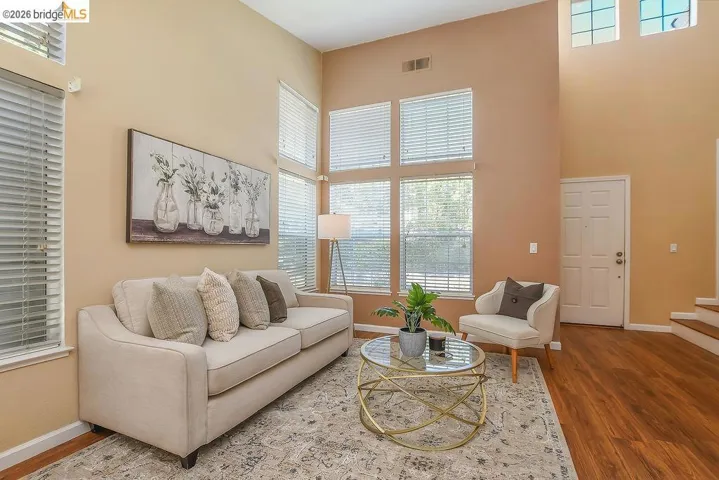 Living area featuring soaring ceilings and high windows with blinds, wood-finish flooring, and a white paneled entry door
