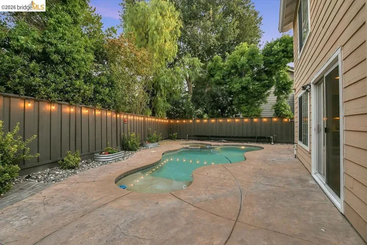 Backyard oasis featuring a curvilinear pool with integrated lighting, stamped concrete patio, and a privacy fence adorned with string lights