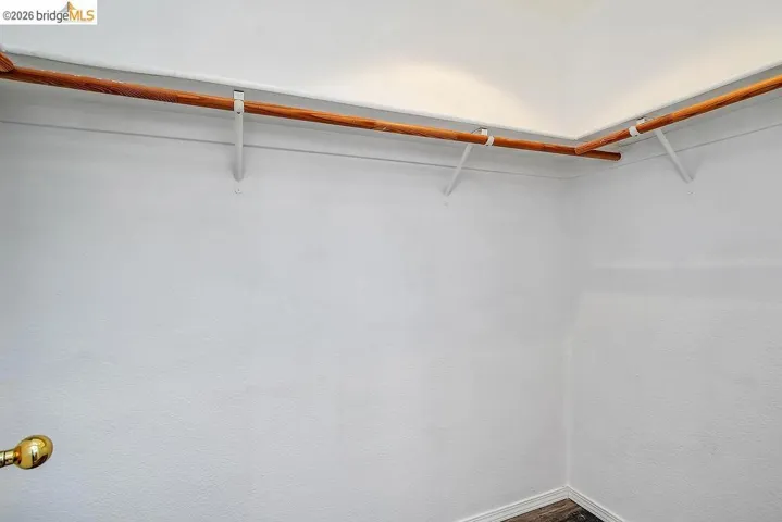 Walk-in closet with white walls, wood-finish flooring, and a brass door handle