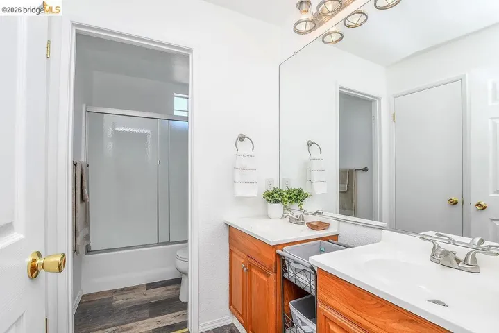 Bathroom featuring a wood-finish vanity with a white countertop and integrated sink, a large wall-mounted mirror, and a tub/shower combination with sliding glass doors
