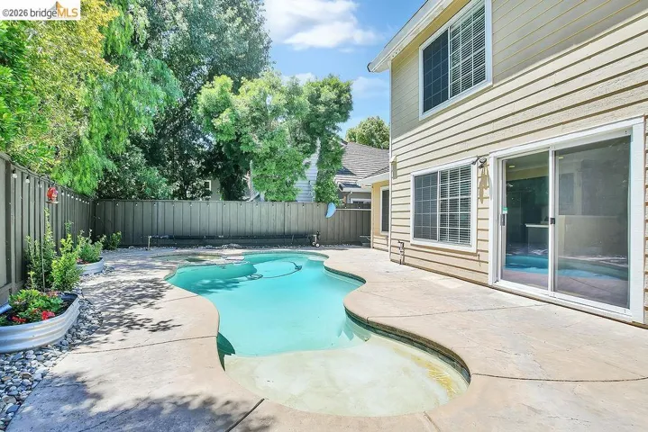 Backyard featuring a freeform swimming pool with integrated spa, concrete decking, and a privacy fence