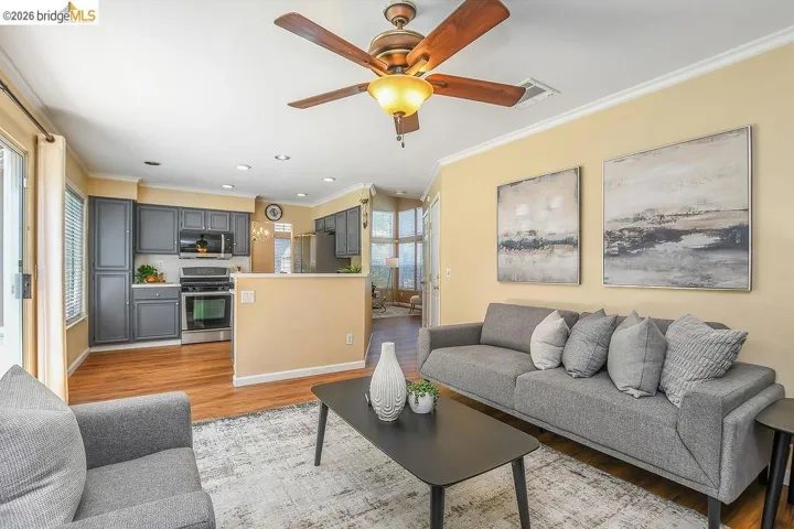 Living room featuring a ceiling fan with integrated lighting, crown molding, and wood-finish flooring