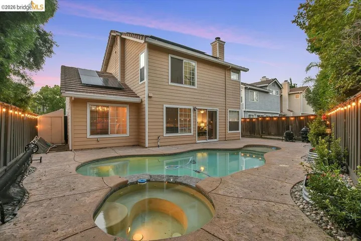 Rear exterior featuring a freeform swimming pool with integrated spa, stamped concrete patio, and mature perimeter landscaping