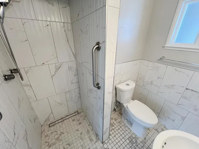 Full bath featuring a marble finish shower, tile walls, light tile patterned floors, and a wainscoted wall