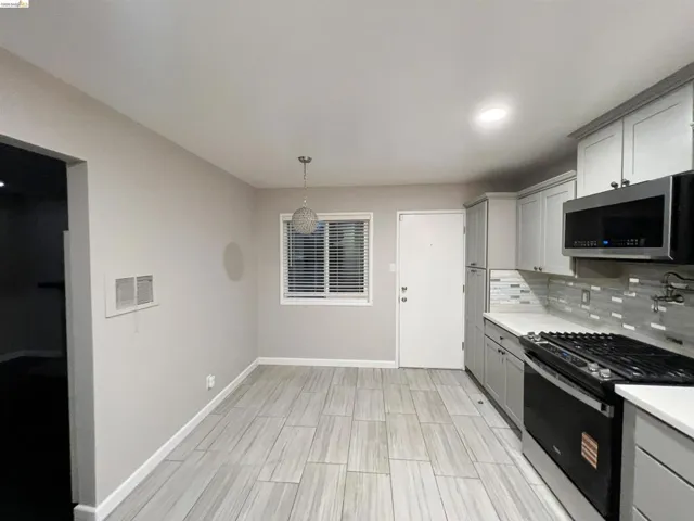 Kitchen featuring gray cabinetry, range with gas cooktop, stainless steel microwave, hanging light fixtures, and tasteful backsplash