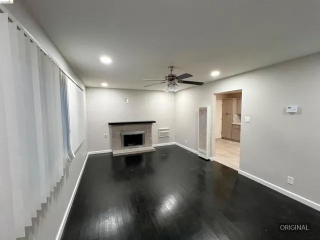 Unfurnished living room featuring a fireplace with raised hearth, dark wood finished floors, a ceiling fan, recessed lighting, and a heating unit