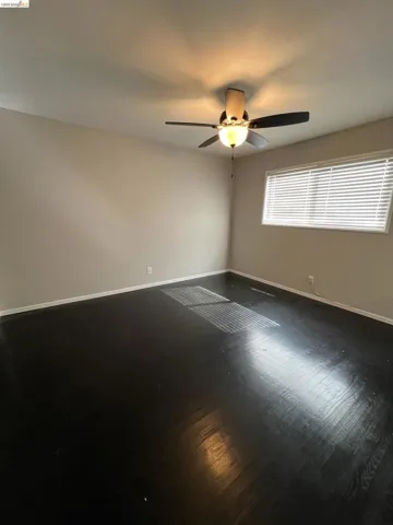 Empty room with dark wood-type flooring and ceiling fan