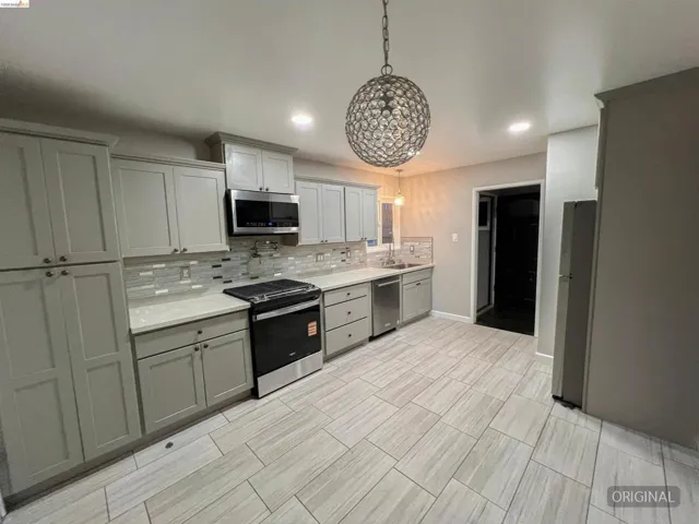 Kitchen with stainless steel appliances, tasteful backsplash, gray cabinetry, light stone counters, and pendant lighting