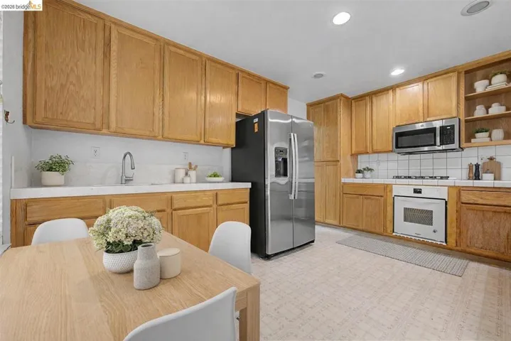 Kitchen featuring open shelves, light flooring, stainless steel appliances, tile counters, and recessed lighting