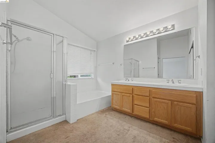 Bathroom with double vanity, a garden tub, lofted ceiling, light carpet, and a stall shower