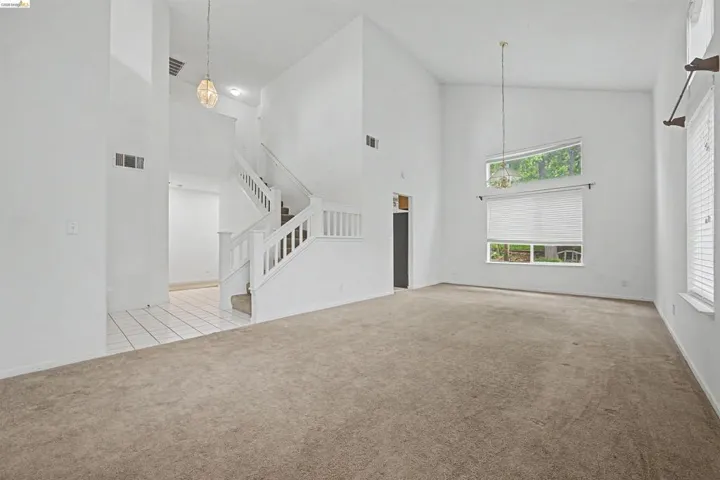Unfurnished living room featuring light carpet, lofted ceiling, and suspended lighting
