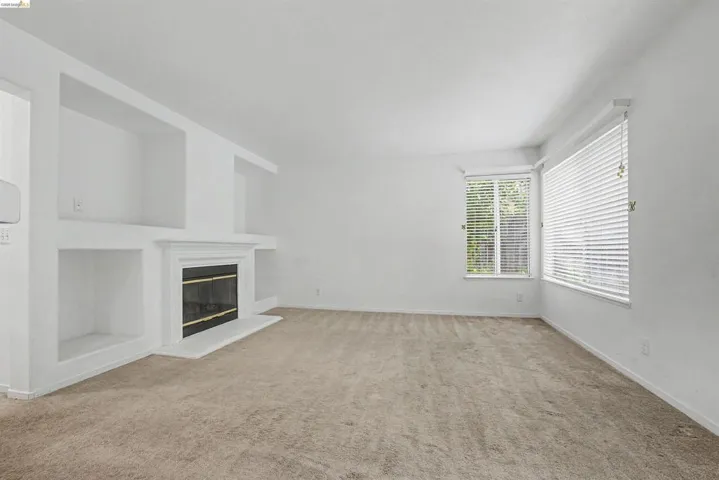 Unfurnished living room with a glass covered fireplace, light colored carpet, and built in features