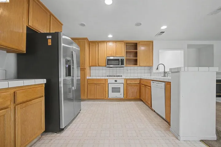 Kitchen with tile counters, light flooring, stainless steel appliances, a peninsula, and decorative backsplash