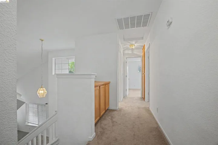 Hallway featuring a textured wall, an upstairs landing, and light colored carpet