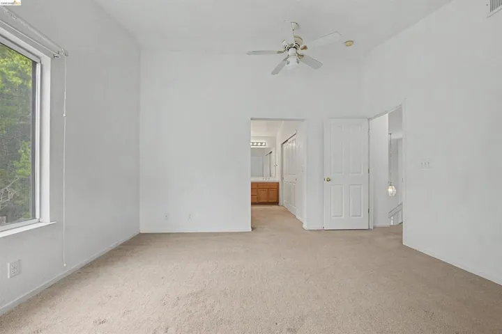 Unfurnished bedroom featuring light carpet, ensuite bath, a ceiling fan, and a high ceiling