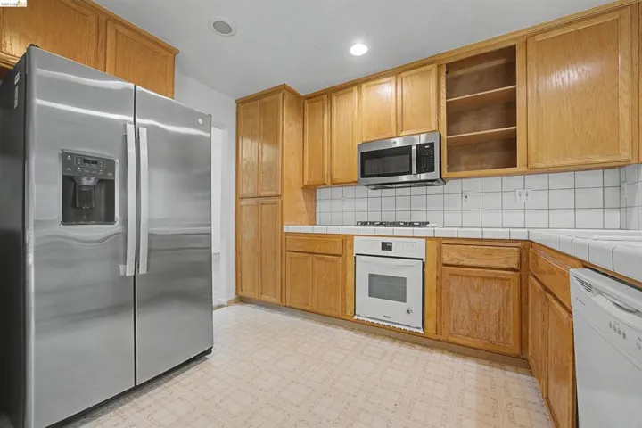 Kitchen with stainless steel appliances, tile counters, open shelves, and tasteful backsplash