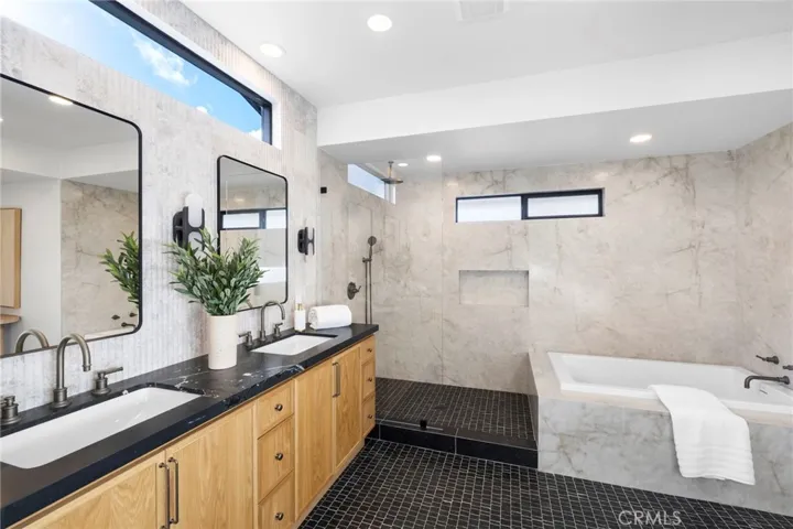 An elegant primary bathroom featuring a spacious slab walk-in shower and a luxurious freestanding bathtub, complemented by custom-designed dual vanity cabinetry and a stunning fluted marble backsplash wall, all contributing to a high-end, spa-like aesthetic.
