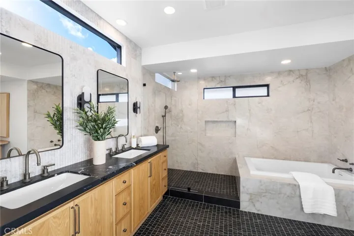 An elegant primary bathroom featuring a spacious slab walk-in shower and a luxurious freestanding bathtub, complemented by custom-designed dual vanity cabinetry and a stunning fluted marble backsplash wall, all contributing to a high-end, spa-like aesthetic.
