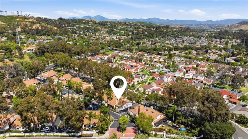Aerial view highlighting the home’s prime location within a well-maintained community, surrounded by mature trees and scenic hills. Showcases proximity to nearby amenities and the overall neighborhood setting.