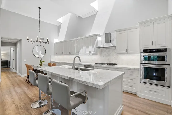Stunning kitchen with oversized island, waterfall-style quartz countertops, shaker cabinetry, and premium stainless steel appliances including double ovens. Clean lines and high-end finishes create a sophisticated and functional culinary space.