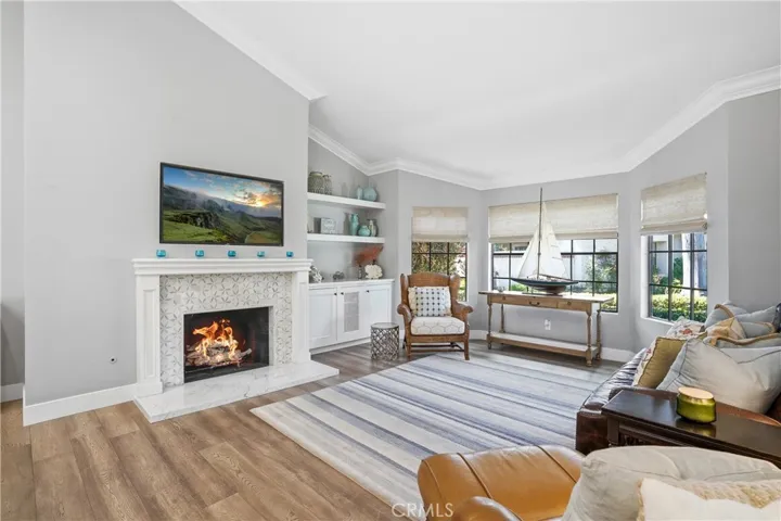 Light-filled living room showcasing vaulted ceilings, large windows, and a cozy fireplace with custom tile detail. The open and airy layout is complemented by natural light, built-in shelving, and warm wood flooring, creating an ideal space for both relaxing and entertaining.