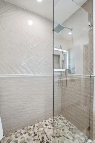 Walk-in shower with glass enclosure, custom tile surround, and pebble stone flooring. Thoughtfully designed with modern finishes, creating a spa-like experience.