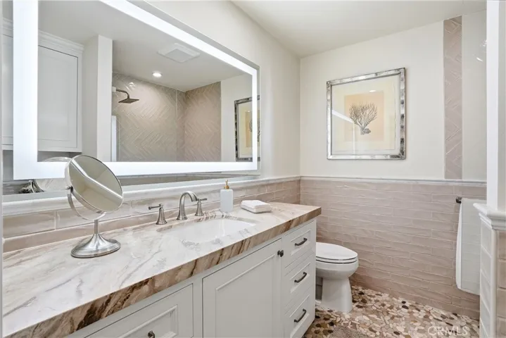 Beautifully updated bathroom with a custom vanity, stone countertop, and modern fixtures. Features designer tile work, illuminated mirror, and a clean, spa-inspired aesthetic.