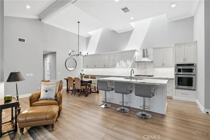 Gourmet kitchen featuring a large center island with bar seating, quartz countertops, custom cabinetry, and stainless steel appliances. Adjacent dining area offers a comfortable space for gatherings, all set beneath dramatic vaulted ceilings with abundant natural light.