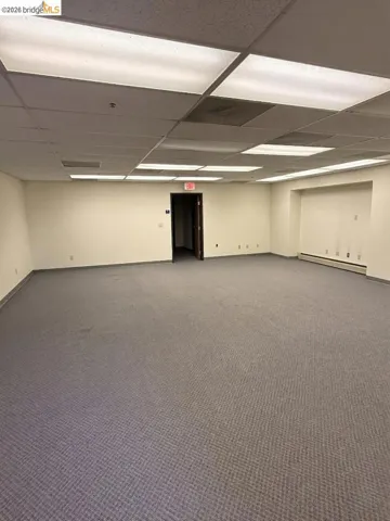 carpeted spare room with a drop ceiling and baseboard heating