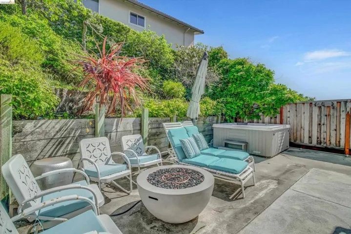 Fenced backyard with a patio area, an outdoor fire pit, and a hot tub