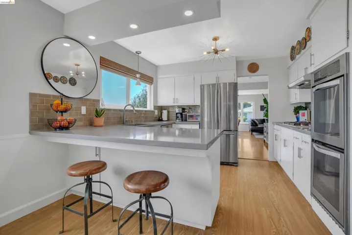 Kitchen with a kitchen bar, white cabinetry, stainless steel appliances, a peninsula, and suspended lighting