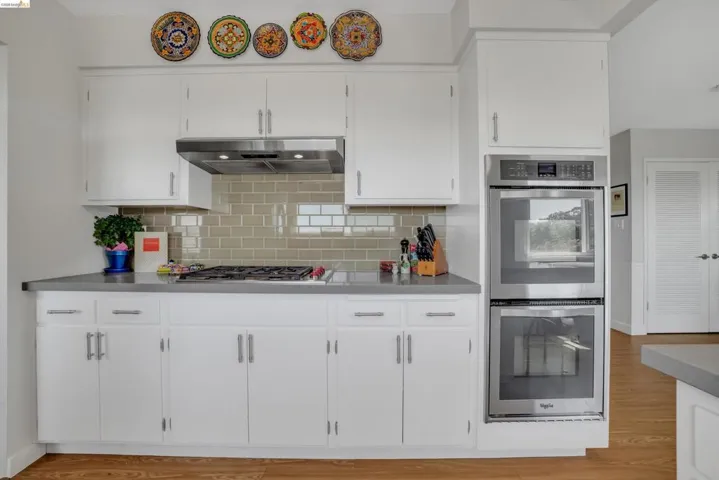 Kitchen with stainless steel appliances, white cabinets, light countertops, backsplash, and light wood-style flooring