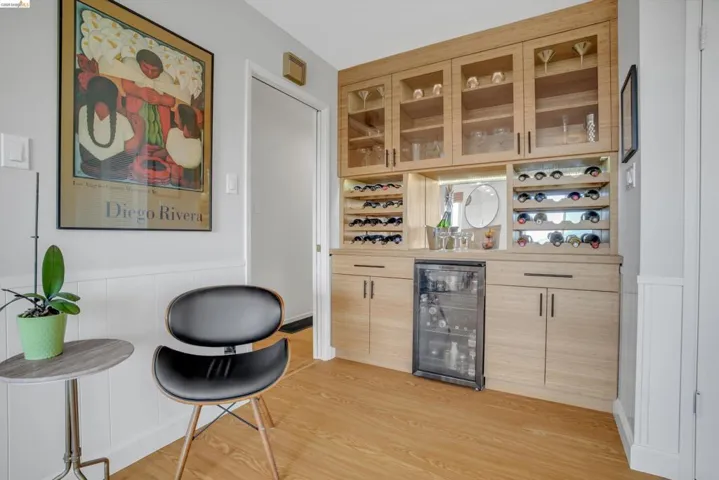 Indoor dry bar with a wainscoted wall, light wood finish cabinetry, light countertops, wine cooler, and glass insert cabinets