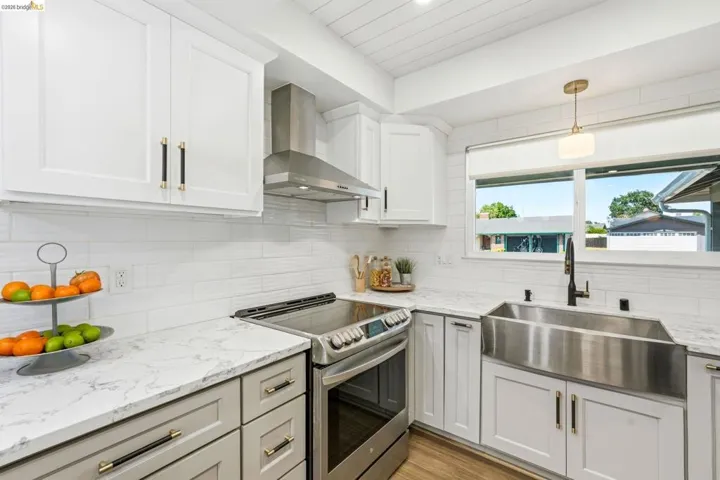 Kitchen featuring electric stove, light stone counters, hanging light fixtures, and white cabinets