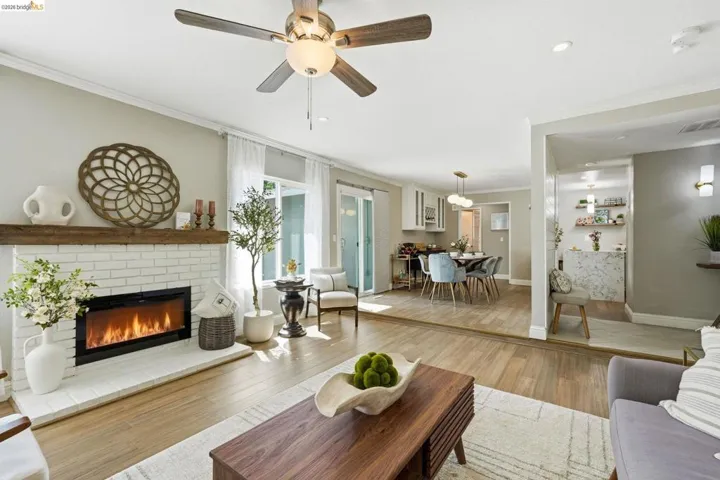Living room featuring ornamental molding, light wood-style flooring, a ceiling fan, a brick fireplace, and recessed lighting