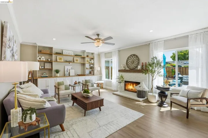 Living room featuring ornamental molding, a ceiling fan, light wood-style flooring, a fireplace, and healthy amount of natural light