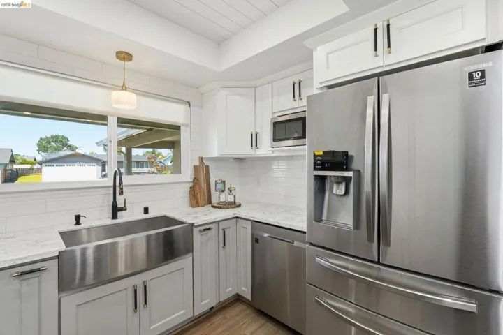 Kitchen featuring stainless steel appliances, light stone countertops, white cabinetry, and light wood-style flooring