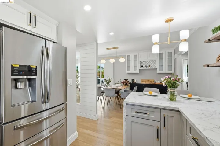 Kitchen featuring stainless steel refrigerator with ice dispenser, light stone counters, light wood-style floors, glass insert cabinets, and hanging light fixtures