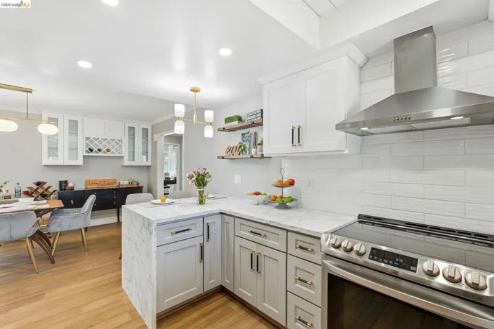 Kitchen featuring stainless steel range with electric cooktop, light stone countertops, light wood-style flooring, a peninsula, and white cabinets