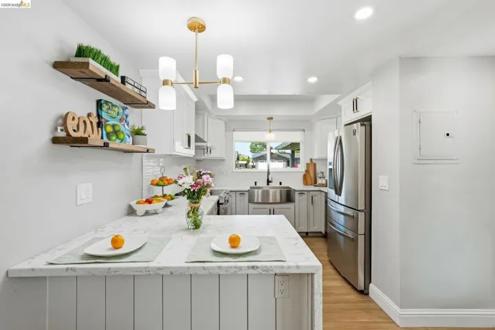 Kitchen with light stone countertops, stainless steel fridge, light wood finished floors, open shelves, and white cabinetry