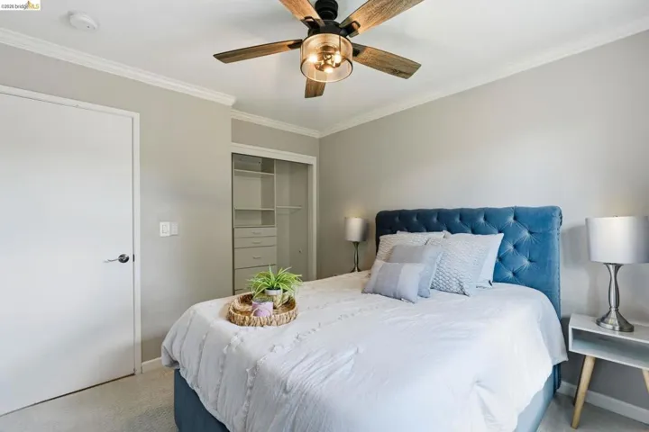 Bedroom with light colored carpet, ornamental molding, a ceiling fan, and a closet