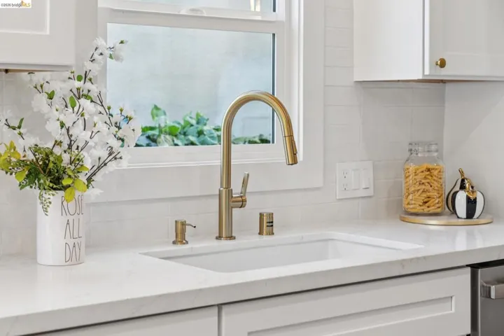 Kitchen view of white cabinetry, light stone counters, tasteful backsplash, and dishwasher