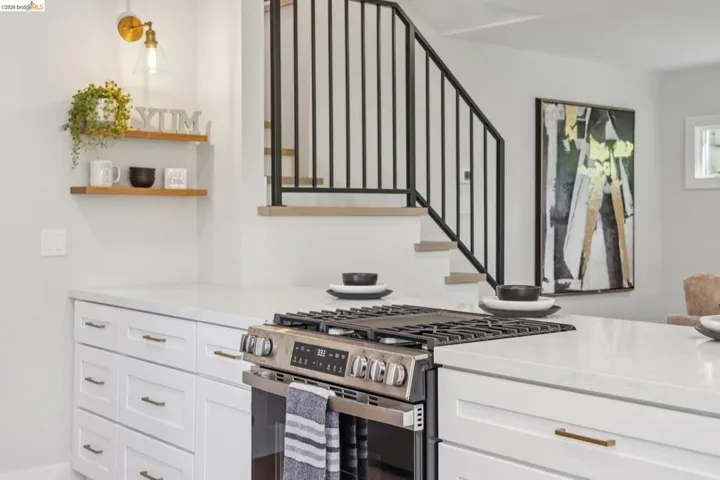 Kitchen featuring stainless steel range with gas cooktop, white cabinets, light stone counters, and open shelves