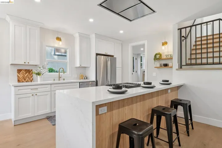 Kitchen featuring a breakfast bar area, range hood, a peninsula, stainless steel appliances, and white cabinetry