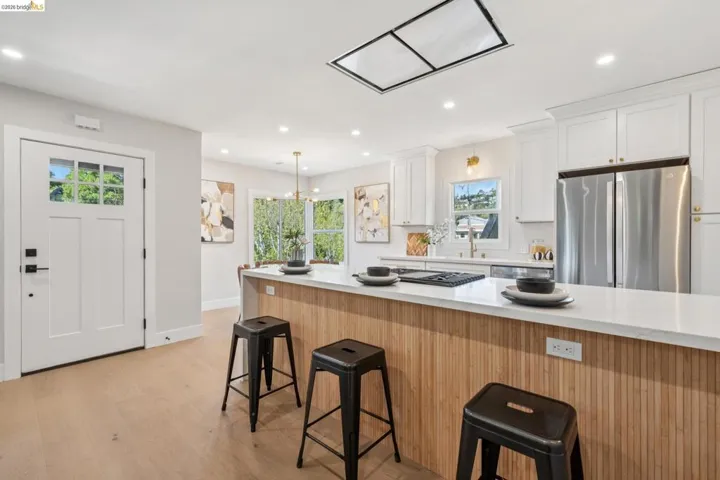 Two tone kitchen featuring a breakfast bar, freestanding refrigerator, light wood finished floors, exhaust hood, and two tone color scheme