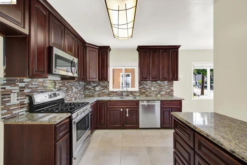 Kitchen with stainless steel appliances, light stone countertops, dark wood finish cabinets, and light tile patterned floors