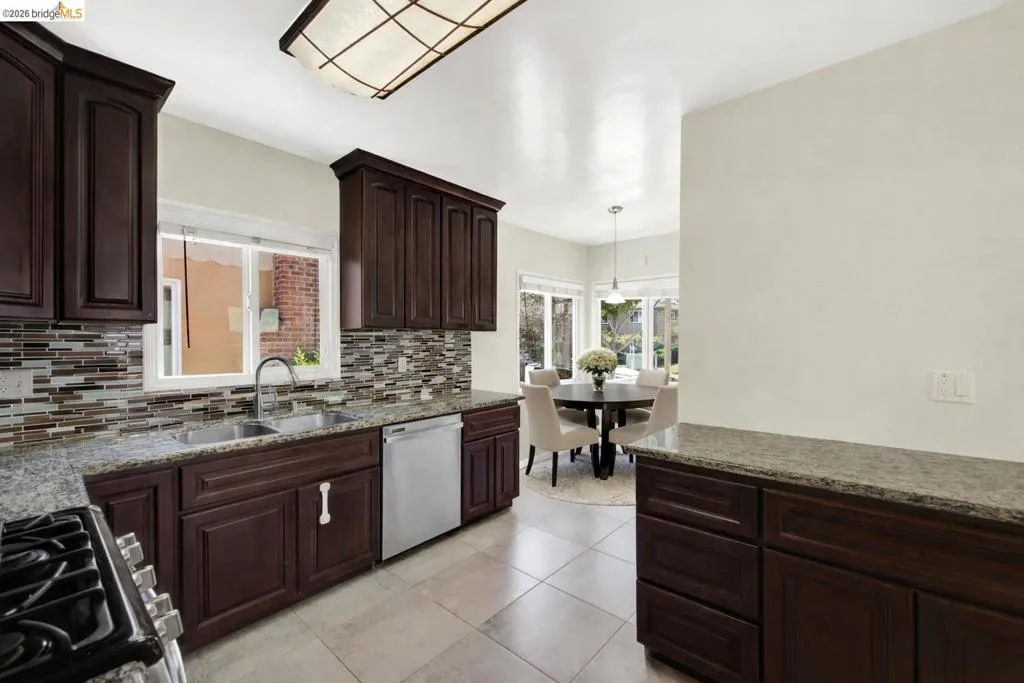 Kitchen featuring dark wood finish cabinets, black gas range oven, stainless steel dishwasher, decorative light fixtures, and light stone countertops