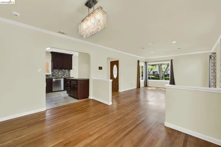 Unfurnished living room with arched walkways, light wood finished floors, ornamental molding, and a chandelier